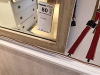 Close-up of mirror frame corner showing textured painted metal finish and beveled glass edge, with dresser reflection in background.