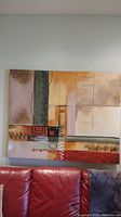 Front view of abstract canvas wall art hung on a wall above a red couch. Shows full artwork and colors.
