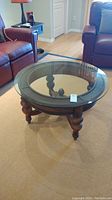 Full view of the round coffee table showing the glass top, wooden base, and surrounding furniture.