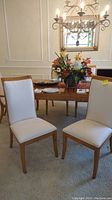 Pair of armless dining chairs with white upholstery and wooden frames positioned near dining table in room setting.