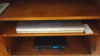 Silver Samsung DVD player DVD-P241 in wooden shelf, front view with buttons visible.