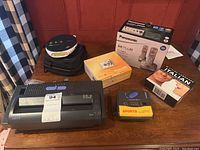 Overview of lot with all electronics items displayed on table, including IBM shredder, Panasonic phones box, Sony Walkman, cameras, and audio tapes