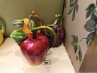 Three ceramic pitchers modeled as red apple, yellow pear, and purple grape cluster, hand-painted, no chips visible