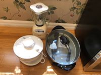 Photo showing Presto electric skillet with glass lid, Osterizer blender, and plastic salad spinner on wooden floor near wall