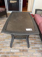 Full view of the plastic rattan patio coffee table with glass top showing surface and legs.
