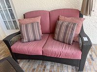 Front view of plastic rattan loveseat with pink cushions and two sets of decorative pillows.