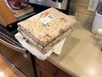 Stack showing folded queen-size floral sheets with beige background and multicolored flowers; other sheets underneath are visible.