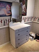 Photo of white solid pine wood four drawer chest with round metal knobs placed in room beside wall with wallpaper and posters