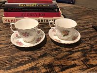 Top view showing both tea cups with saucers on wooden surface, floral designs visible.