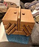 Closed wooden accordion-style sewing basket showing natural wood finish and wooden knob handles.