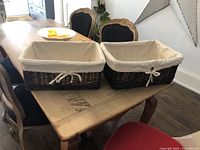 Two dark brown wicker baskets with beige linen liners tied at front, sitting on wood table