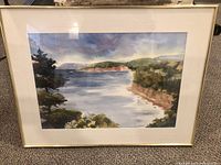 Full view of the framed watercolour coastal landscape painting showing the trees, water, cliffs, and hills