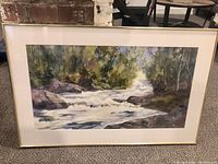 Full view of framed watercolour painting depicting a rushing stream in a natural wooded setting.