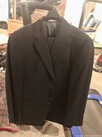 Dark men's suit jacket hanging on a hanger, front view showing two-button closure and notch lapel.