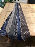 View of seven men's ties laid on table, showing different patterned designs in blue, gray and beige tones
