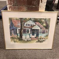Framed watercolour painting depicting a Wards Island home, showing a front view of the house with two white chairs on the lawn.