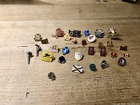 Wide view of 28 assorted pins and charms displayed on a wooden surface, showing a variety of designs and themes including sports teams, promotions, and decorative elements.