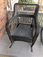 Front view of black resin wicker rocking chair showing wicker weave seat, arms, and rocker base