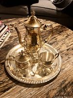 Full view of the tea service on round silver serving tray including teapot, creamer, and sugar bowl with lid