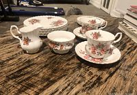 Full set showing all pieces on wooden surface including plates stacked, two teacups on saucers, cream jug and sugar bowl.