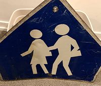 Front view of the vintage school crossing sign showing blue background and white children figures holding hands.