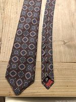 Full view of the vintage Yves Saint Laurent silk tie laid flat on a wooden surface, displaying the overall pattern and pointed end.