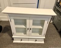 White wood medicine cabinet front view showing closed double glass-panel doors and two drawers below.