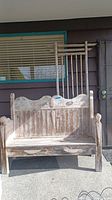 Front view of wood porch bench showing carved details on backrest and arms, weathered finish.