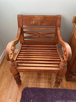 Front view of the carved wood chair showing slatted seat and backrest with carved detail.