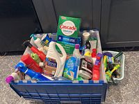 Full view of plastic basket filled with assorted cleaning supplies including Cascade Complete, Bona floor cleaner, Weiman spray cleaner, and various other bottles and scrubbers