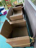 Side view of three stacked brown plastic rattan patio chairs showing armrests and open seating area.