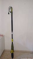 Full view of the electric pole saw showing entire length and extendable shaft, green and yellow coloring.
