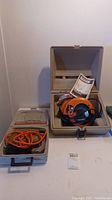 Orange and black Skilshop 7.25 inch skill saw in gray carrying case with manual, alongside a separate case with orange cord visible.