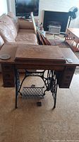Full view of antique Singer sewing machine in a wooden cabinet with drawers and foldable top, sitting on a floor next to a couch.