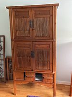 Front view of wooden cabinet with vertical slat doors and metal handles, showing two upper doors, two lower sliding doors with one stuck, and three bottom drawers.