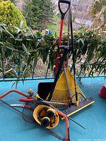 Overview of the lot showing shovel, rake, broom, two hand saws and helmet stacked together.