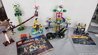 Two complete Lego Batman sets displayed with instruction manuals and minifigures included. The first set is Joker Manor with clown-themed structures and figures. The second set is Catwoman Catcycle Chase with a motorcycle and figures of Batgirl, Robin, and Catwoman.