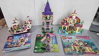 Three assembled Lego Disney Princess sets and their instruction manuals. Ariel's Underwater Castle on right, Rapunzel's Tower in center, Snow White's Boat on left.