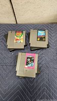 Three Nintendo NES game cartridges: Magmax, Kung Fu, Dragon Spirit on quilted mat
