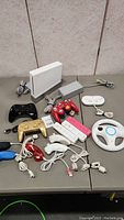 Wii console, multiple controllers, accessories, and cables displayed on gray table.