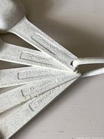 Set of six speckled plastic measuring spoons with Tupperware branding, connected by a plastic ring, shown fanned out.