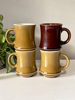 Four ceramic mugs stacked two on two, showing mustard yellow and reddish-brown colors.