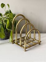 Side angle showing solid brass structure with three rounded arches and grid base, with a green plant in background.