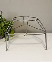 Full side view of the vintage metal raised plant pot holder showing the circular top and angled legs lifting the pot holder above surfaces.