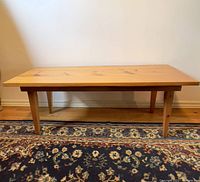 Full front view of the rectangular wooden coffee table on a patterned rug against a white wall.