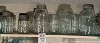 Front view of nine antique glass canning jars arranged on a shelf showing variety of sizes and metal lids on some jars