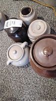 Five pottery jars and jugs arranged on carpet floor, showing various lids and spouts