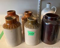 Photo showing five stoneware jars with beige bodies and varying brown and green glazed tops, one marked with green sticker '4x6.5'