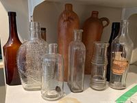 Front row and back row of various vintage bottles including embossed 1883 locomotive and amber ceramic jug.