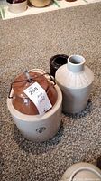 Photo of the Medicine Hat crock with lid and metal clasp, and two jars displayed on carpet